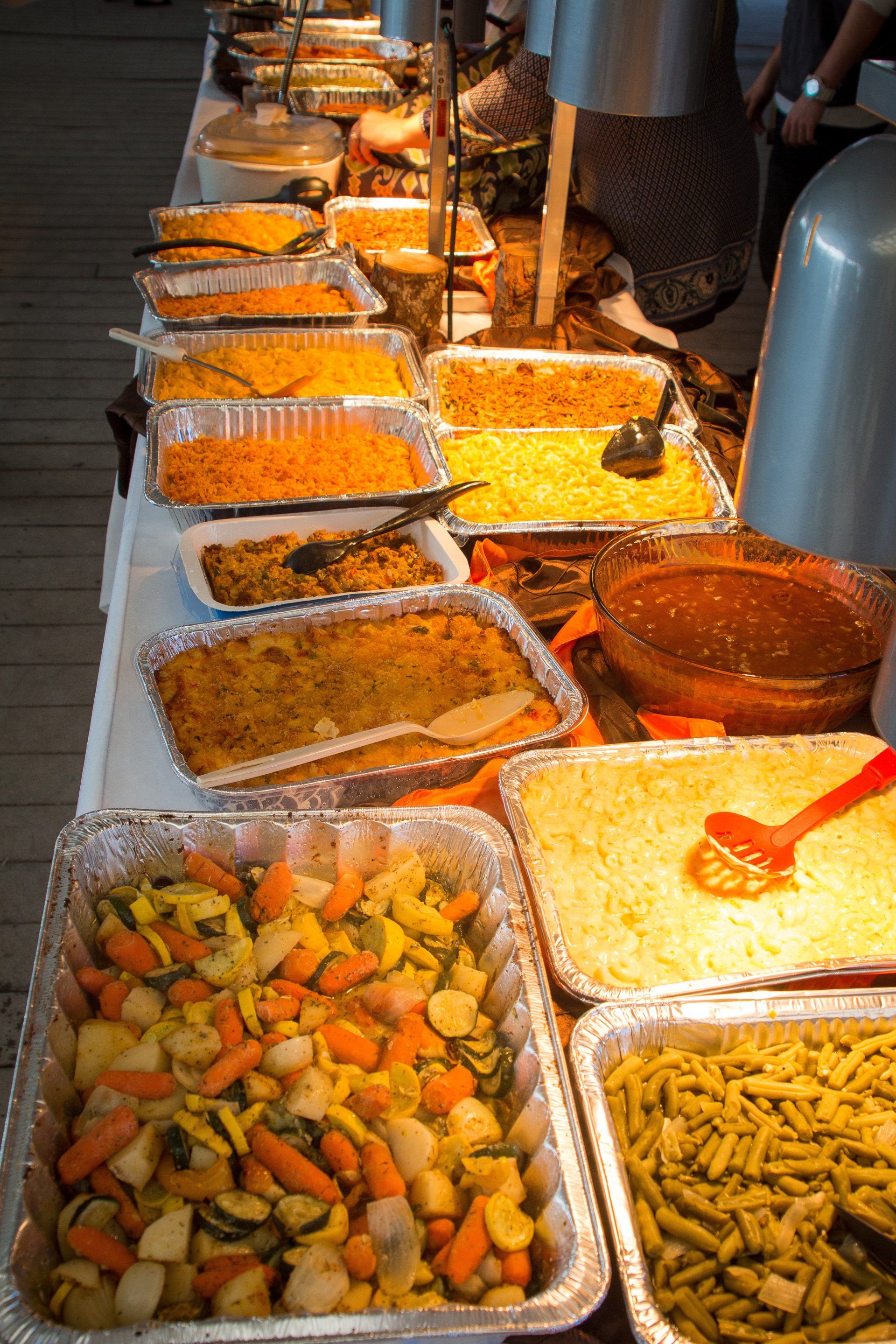A buffet table lined with rows of aluminum catering trays filled with various prepared dishes and vegetables.