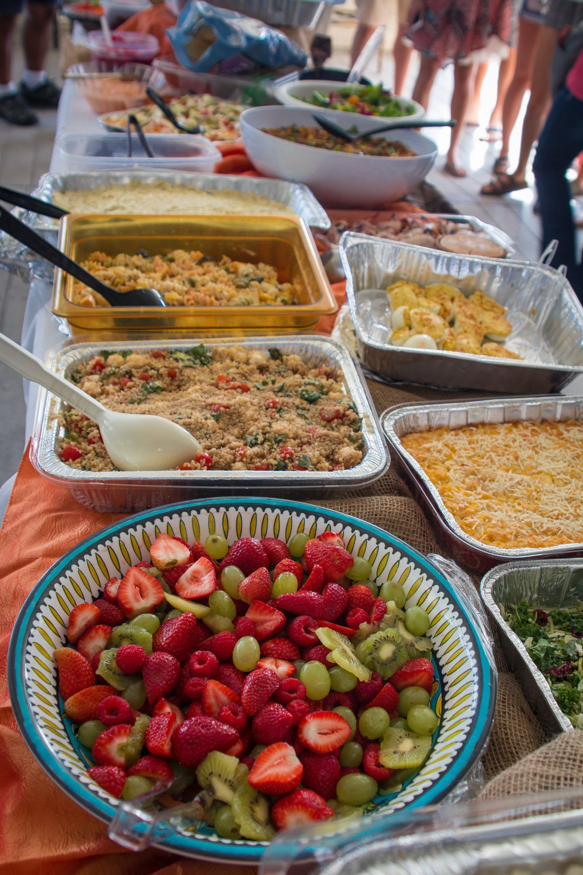 A buffet table lined with various dishes, including a large bowl of fruit salad, pasta, and baked casseroles.