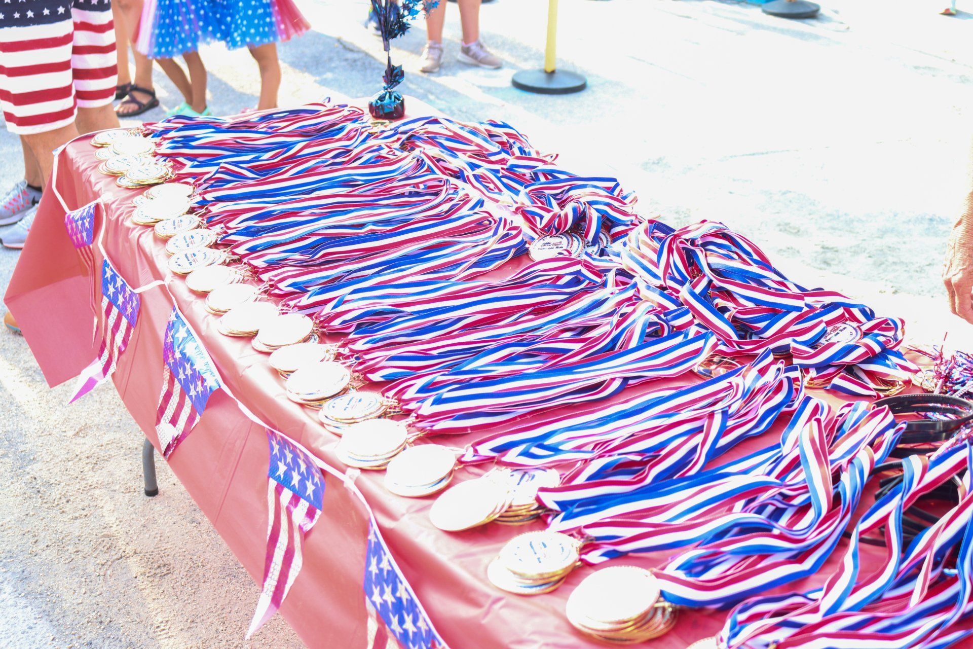 A table covered in a red cloth, decorated with American flag buntings and loaded with rows of medals on red-white-blue ribbons.