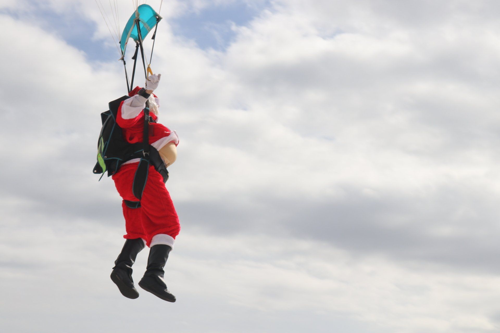 A person dressed as Santa Claus skydiving against a backdrop of a cloudy sky.