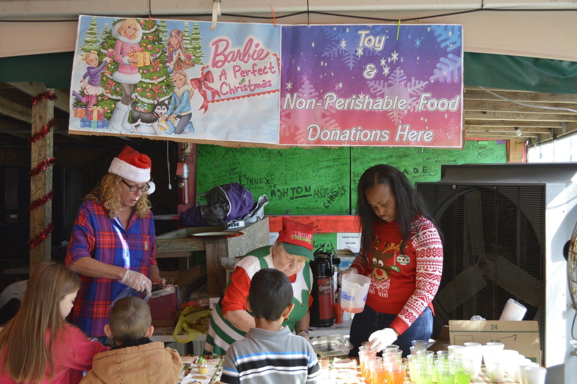 A food donation booth with two banners, one featuring Barbie and the other requesting non-perishable food donations.