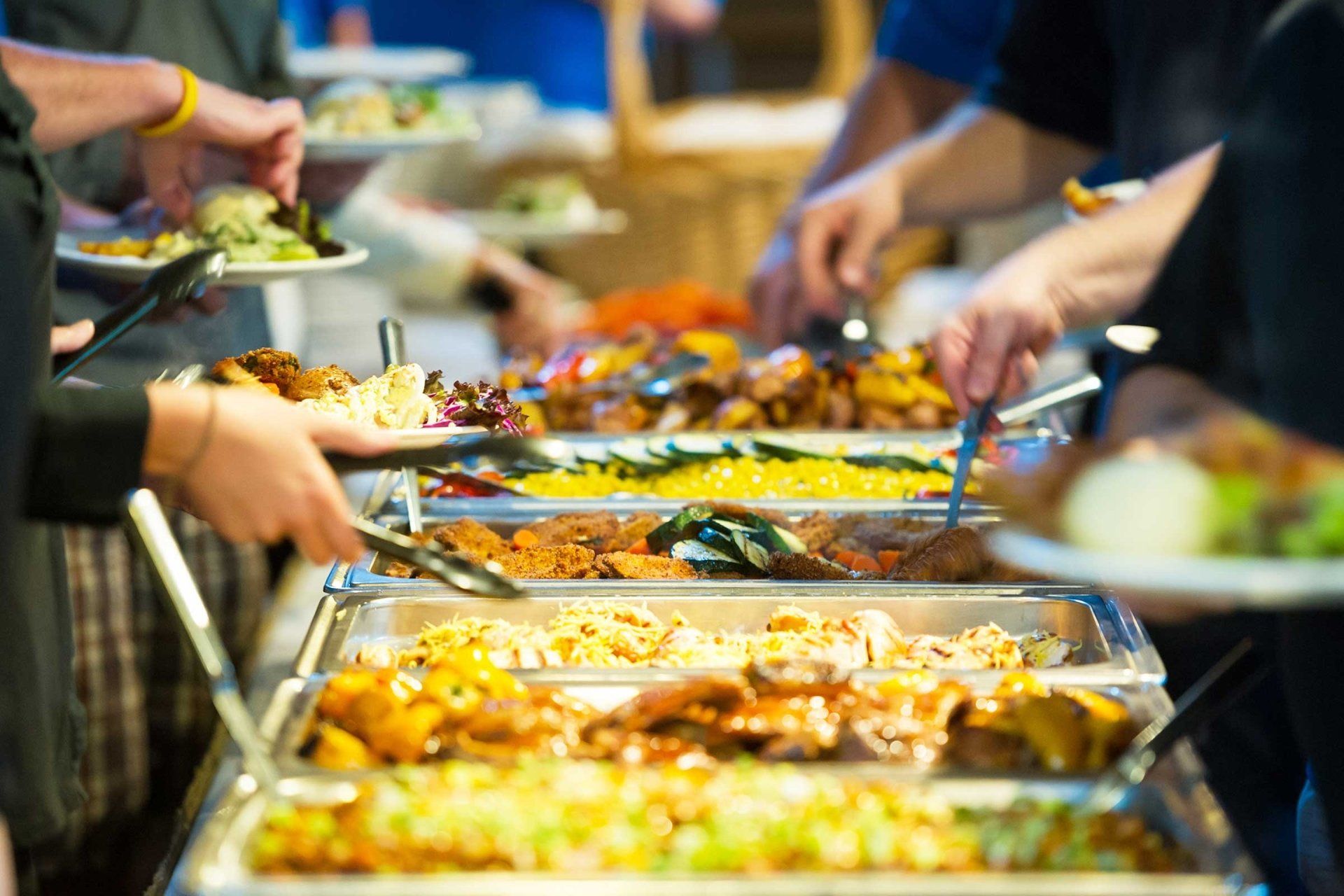 People serving themselves from a buffet line featuring various warm dishes in metal trays.