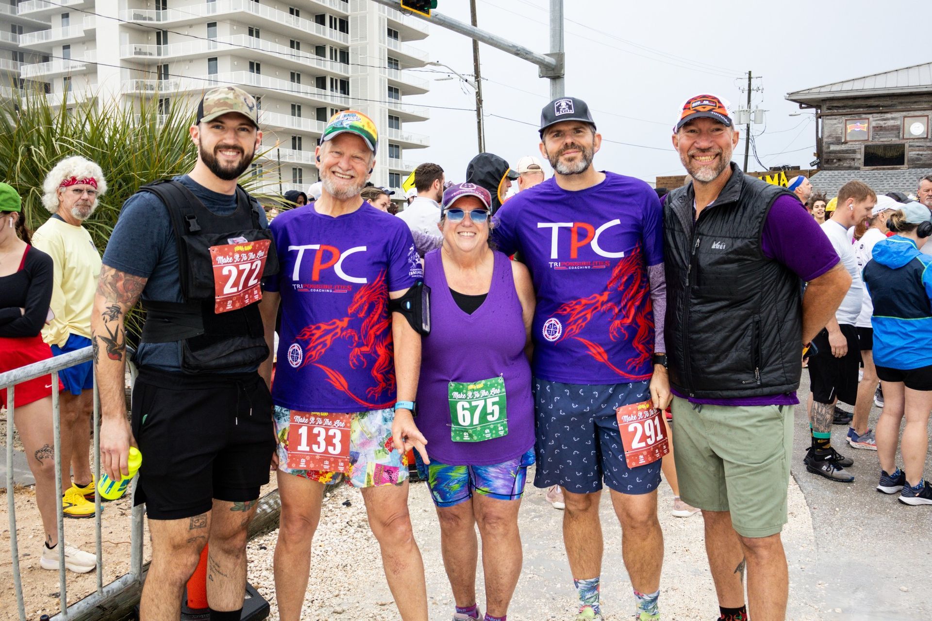 A group of five people wearing race bibs stand together outdoors on a sunny day after participating in a running event.