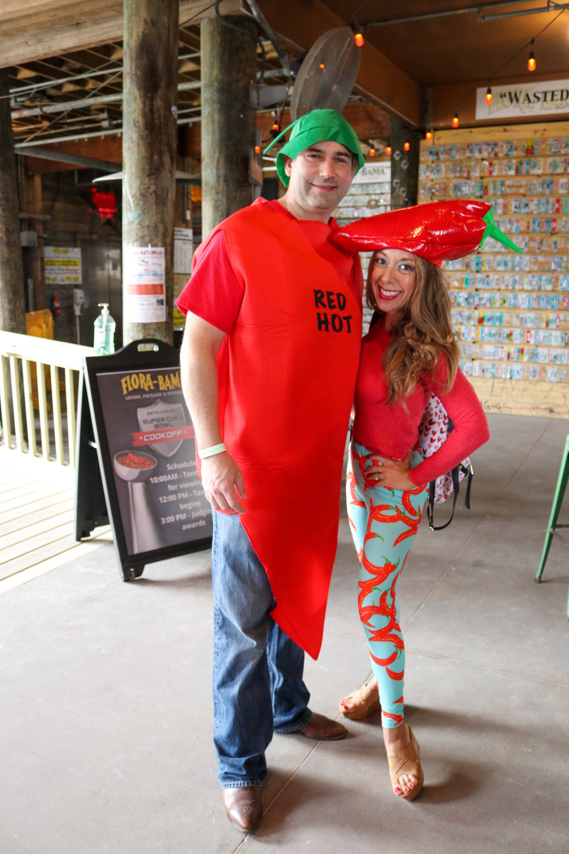 A man and woman in pepper-themed costumes and hats stand smiling together inside a restaurant.