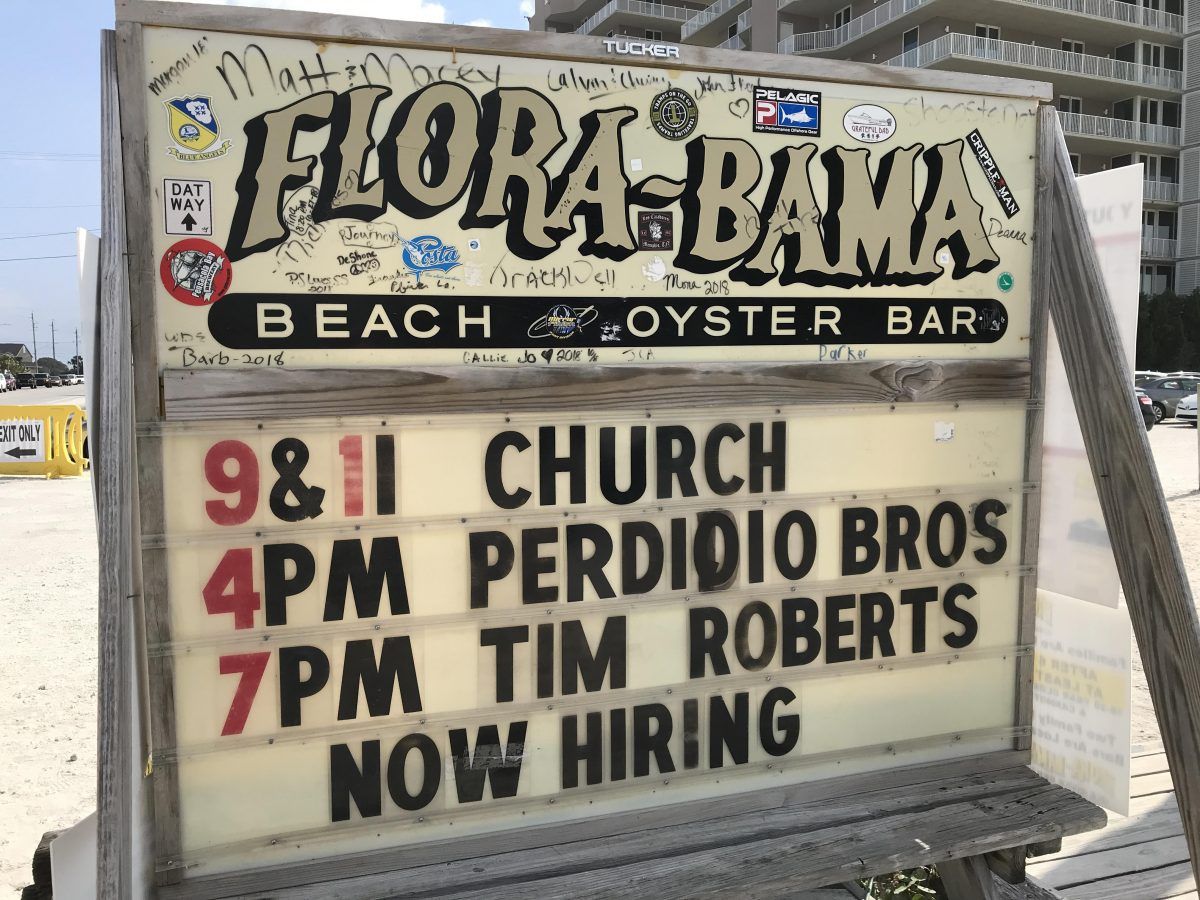 A Flora-Bama Beach Bar sign lists church at 9 & 11, Perdido Bros at 4pm, Tim Roberts at 7pm, and that they are hiring.