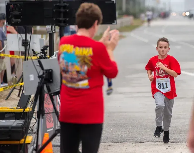 A person in a red shirt cheers for a runner wearing bib number 811, who is approaching a finish line setup on a road.