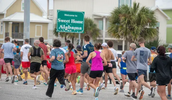 A diverse group of runners participating in a road race past a sign that reads