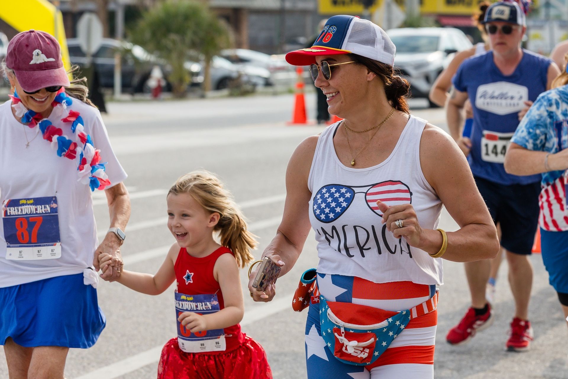 Three people in red, white, and blue festive gear run together outside during a race.