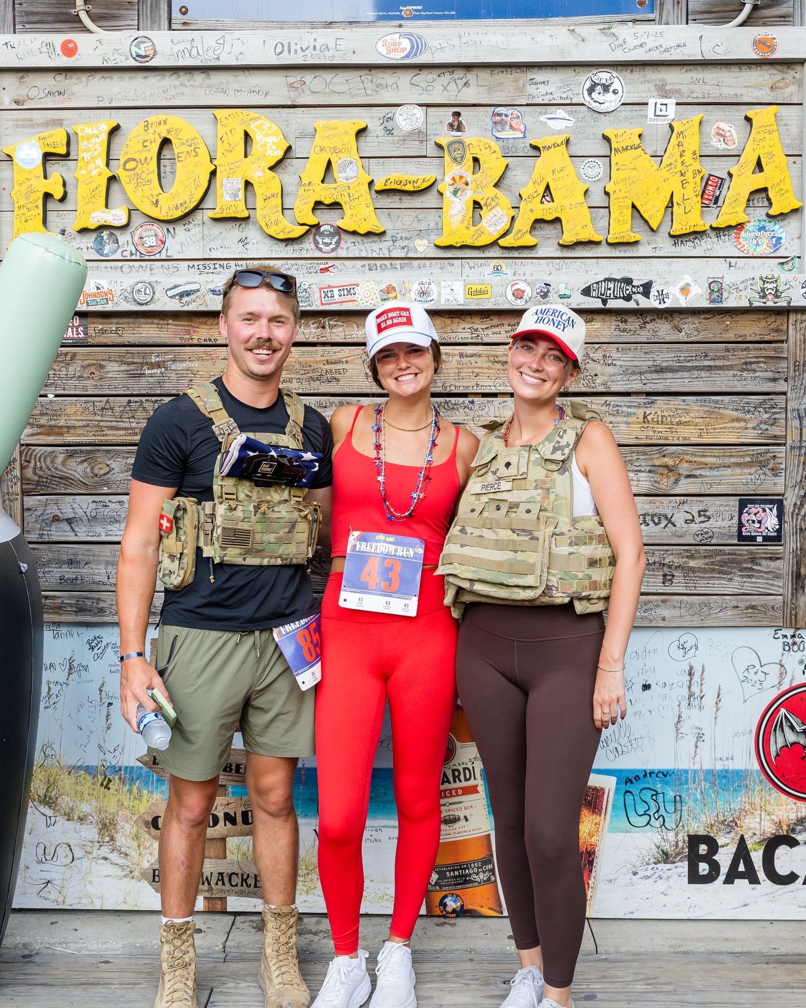 Three people wearing tactical vests stand in front of a wood-paneled wall with a yellow 