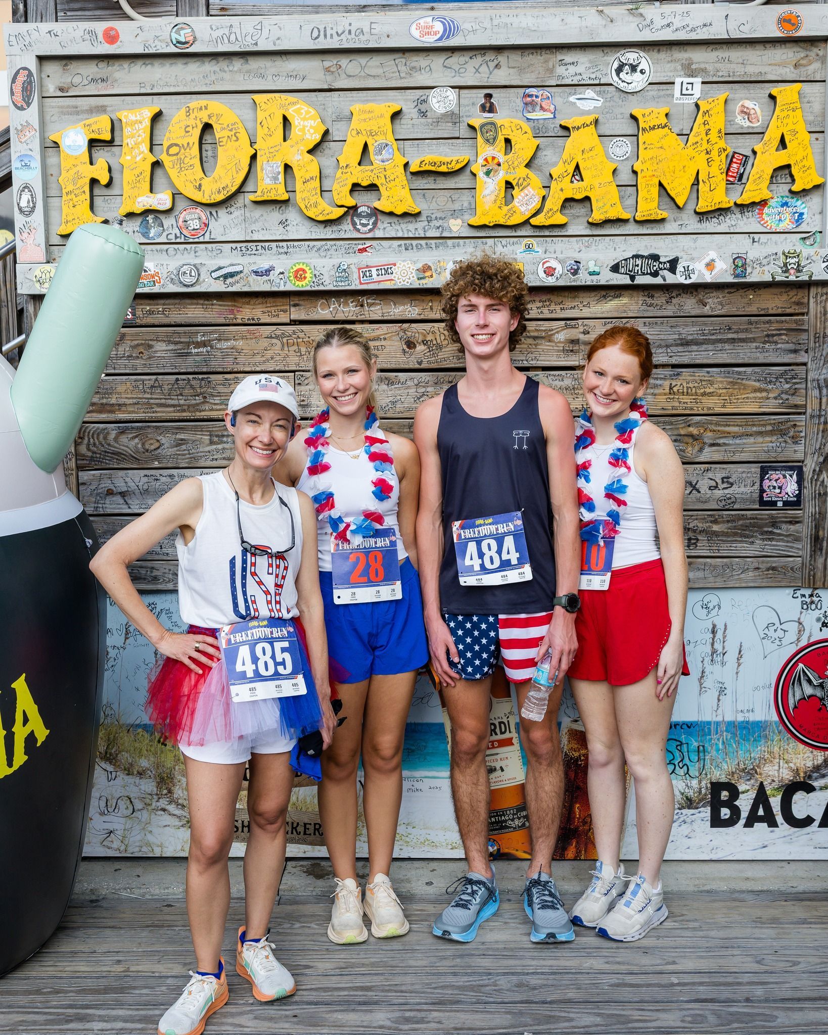 Four people stand in front of a Flora-Bama sign, wearing patriotic-themed running clothes and race bibs.