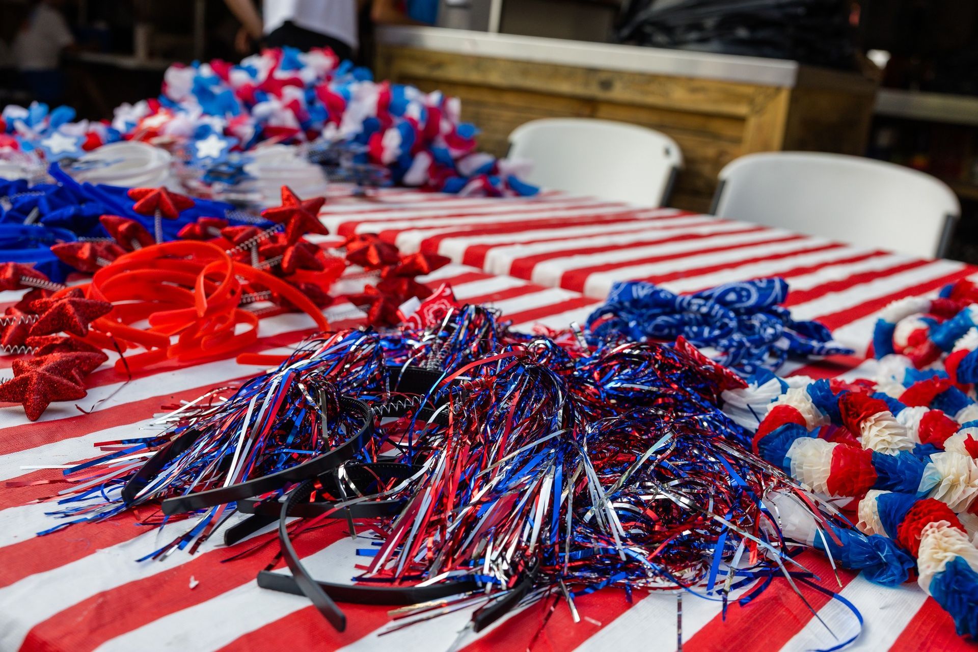 A table covered in a red and white striped cloth is piled with red, white, and blue festive party accessories.