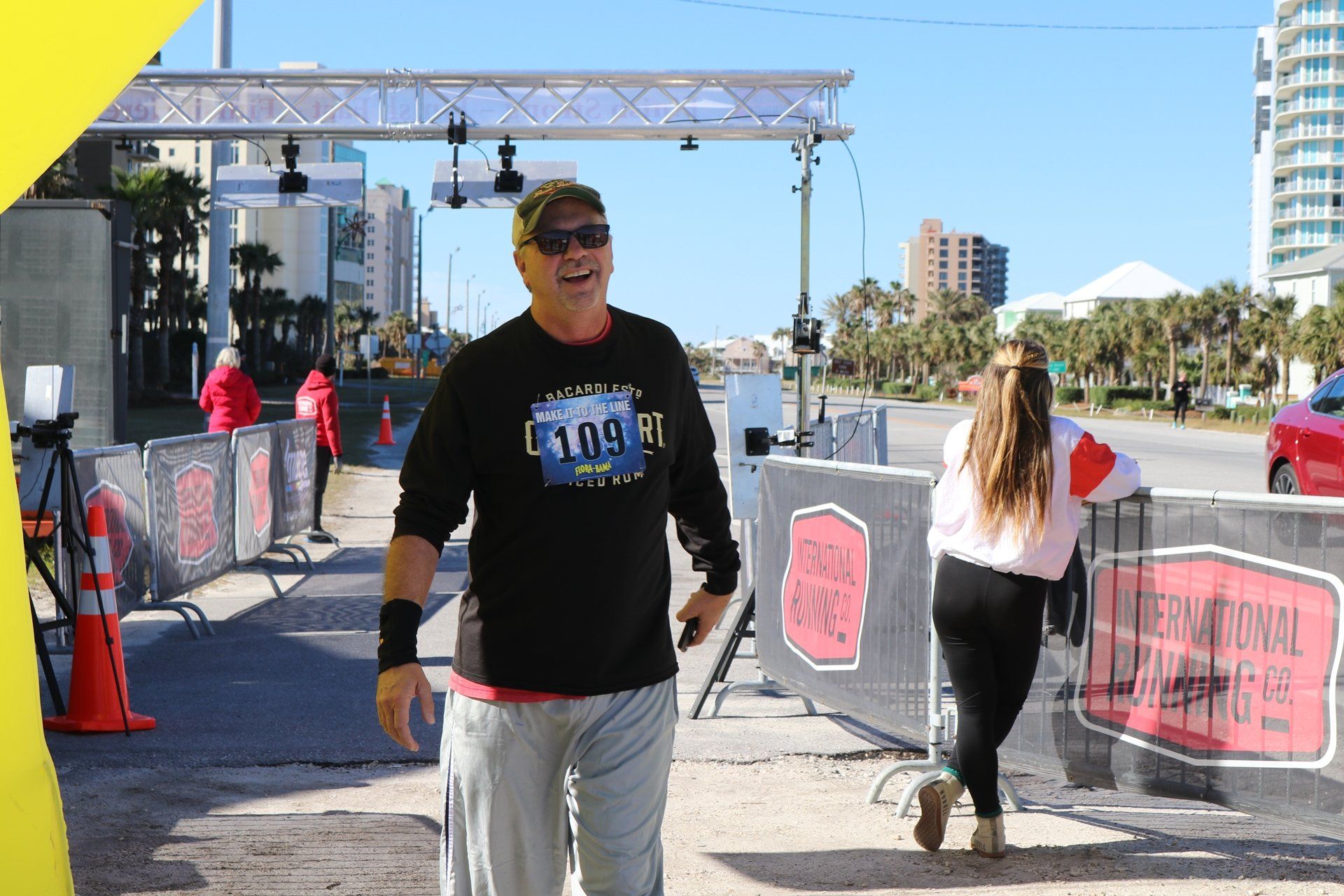 A smiling person in a black long-sleeve shirt with the number 109 walks through an outdoor race finish line.