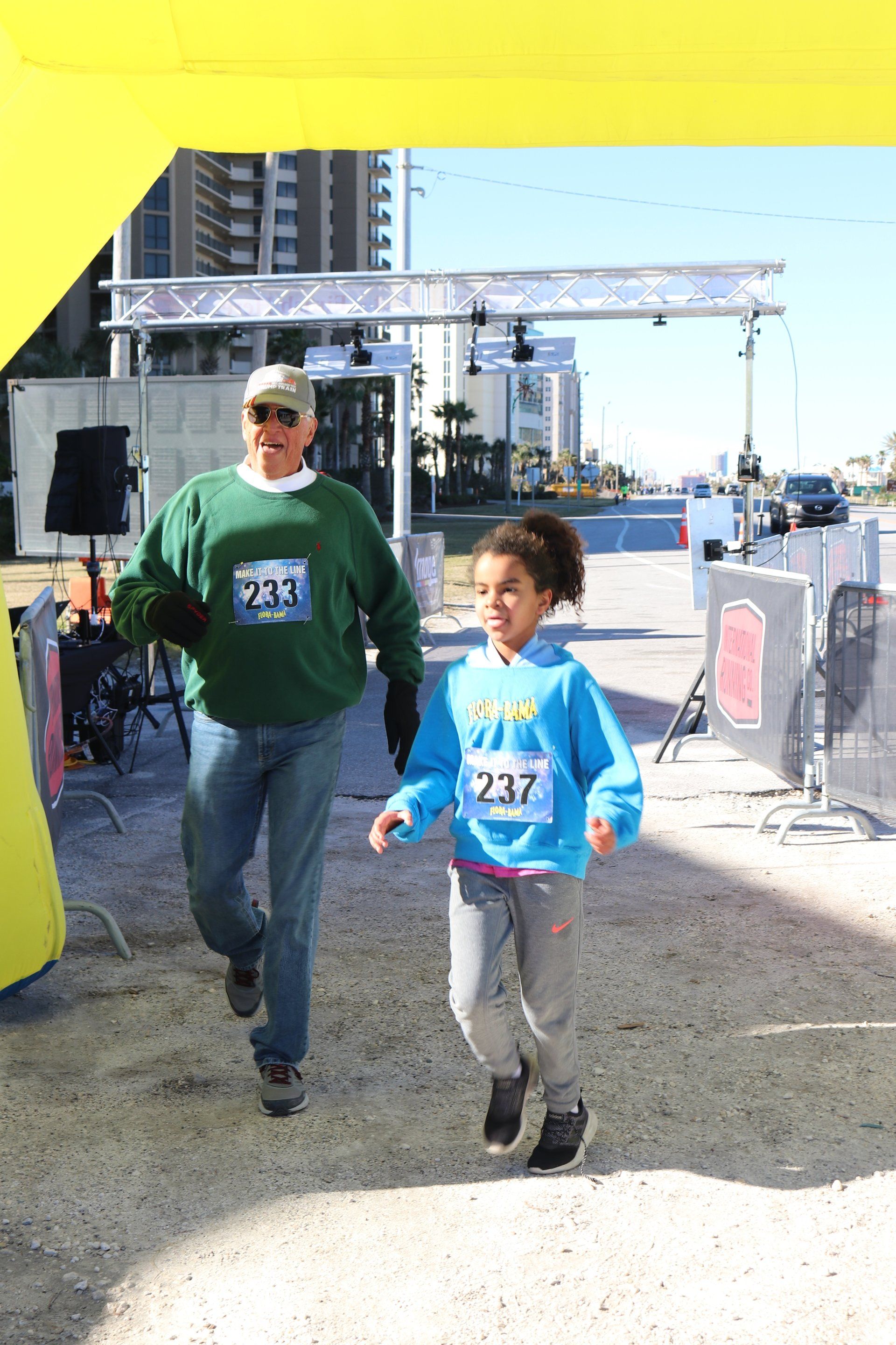 A person in a green sweater and a child in a blue hoodie running together at an outdoor race event.