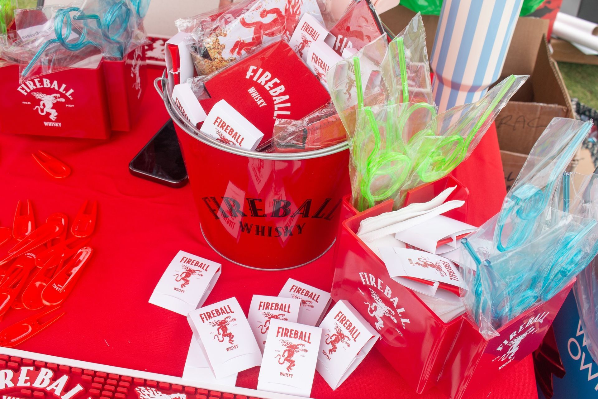 A bright red table setup featuring Fireball Whisky branded merchandise, including buckets, boxes, and small favors.