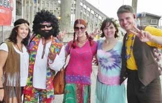 Five people in colorful 1970s-themed outfits posing and smiling outdoors.