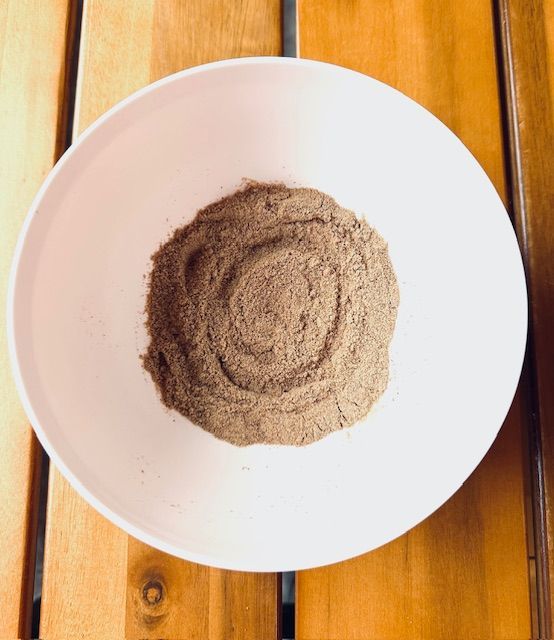 Brown powder in a white bowl on a wooden table.