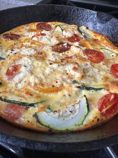 Frittata with zucchini, tomatoes, and cheese baked in a cast iron skillet.