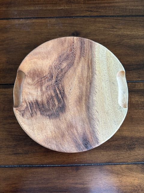 Circular wooden serving tray with handles, resting on a brown wooden surface.