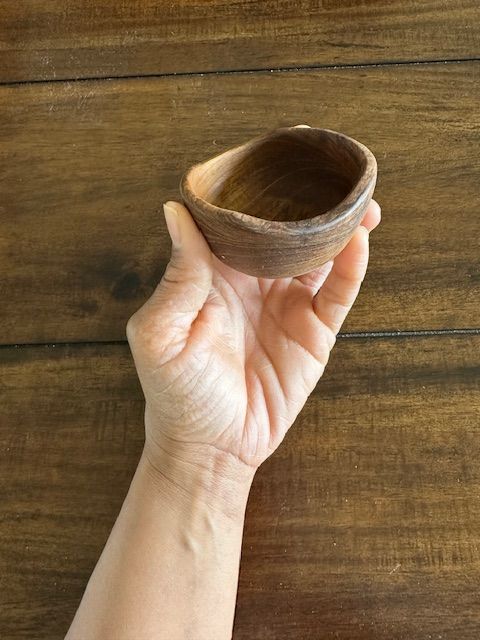 Hand holding a small, wooden bowl against a wooden table.