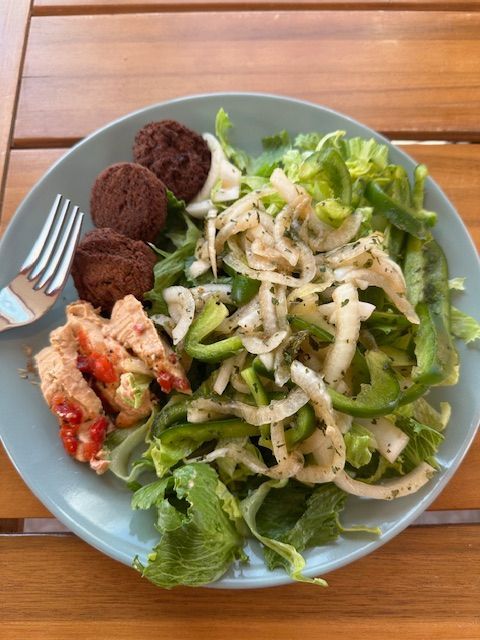Plate of salad with falafel and hummus on a wooden table, green and white vegetables.