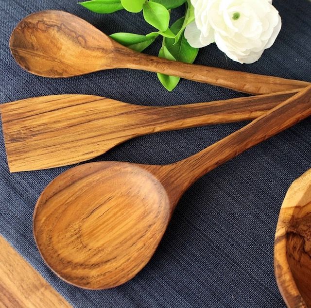 Wooden kitchen utensils: spoon, spatula, and serving spoon on a dark blue cloth, with a white flower and green leaves.