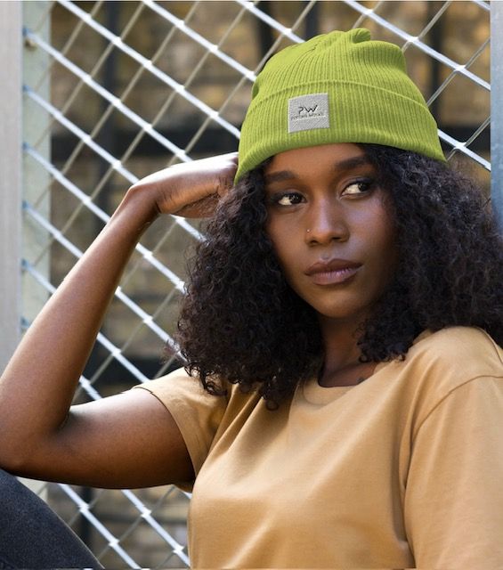 Woman wearing a green beanie and tan shirt, leaning against a metal fence.