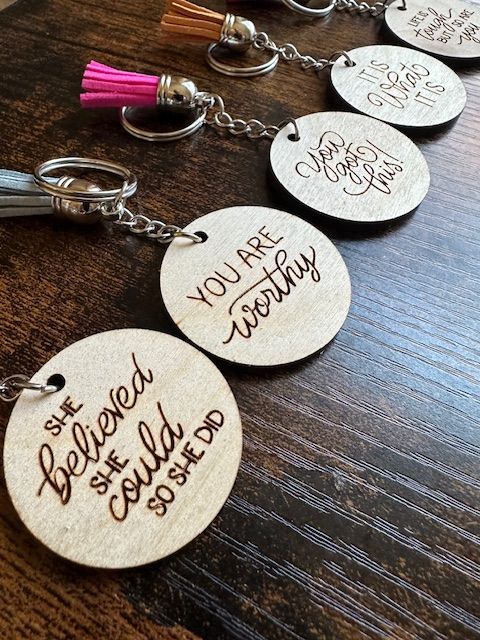 Close-up of engraved wooden keychains with positive quotes and colorful tassels on a wooden surface.