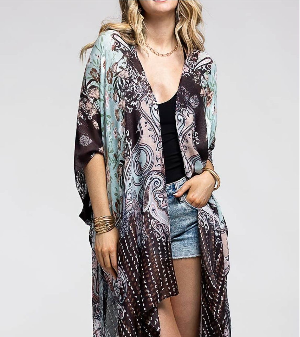 Woman wearing a patterned, long kimono over a black top and jean shorts.