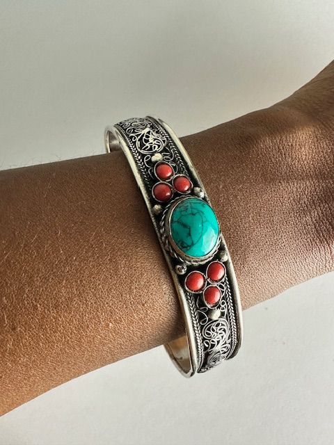 Silver bracelet with turquoise and red coral stones on a dark skin wrist.