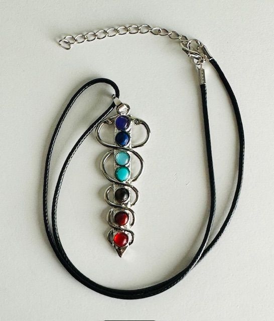 Chakra pendant necklace with seven colorful gemstones, connected by silver metal on black cord.