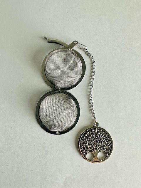 Open stainless steel tea ball with mesh interior and tree of life charm.