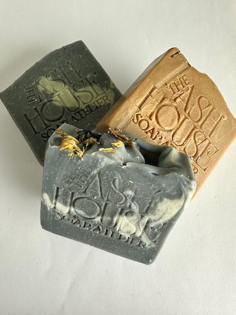 Three artisanal soap bars in shades of gray, brown, and gold, stacked together.