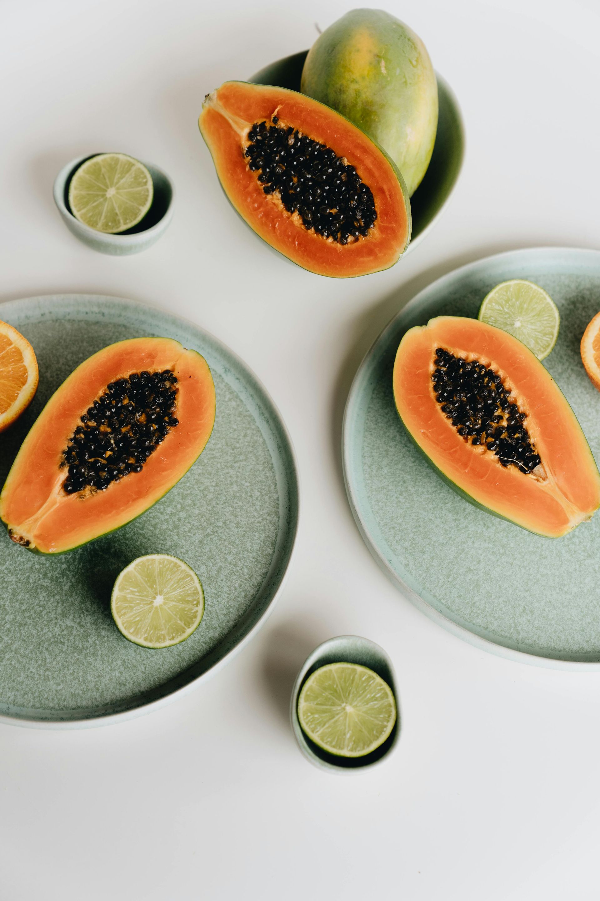 Papayas on plates with limes and orange slices on a white surface.