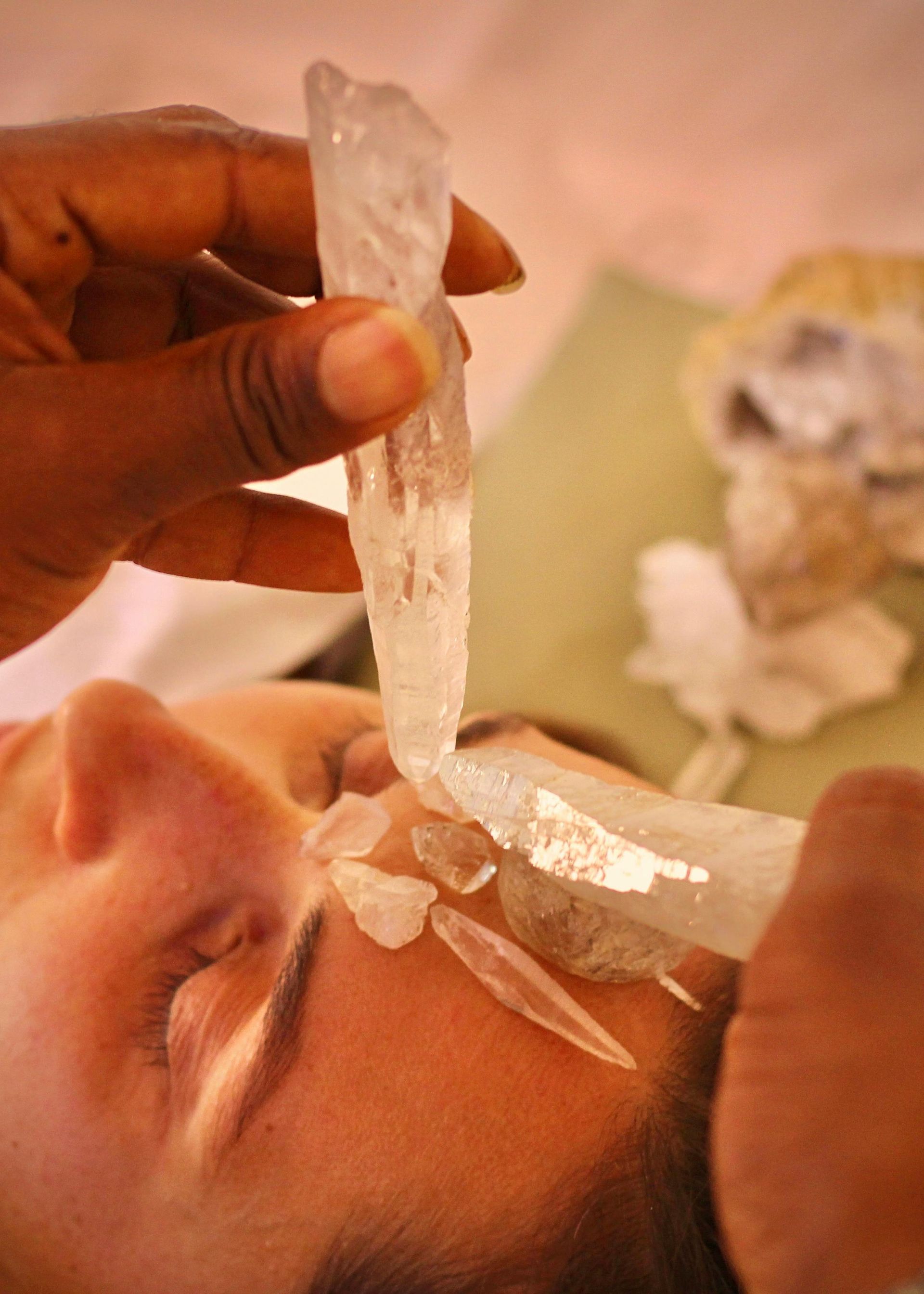 Person receiving crystal healing treatment, holding crystals over face.