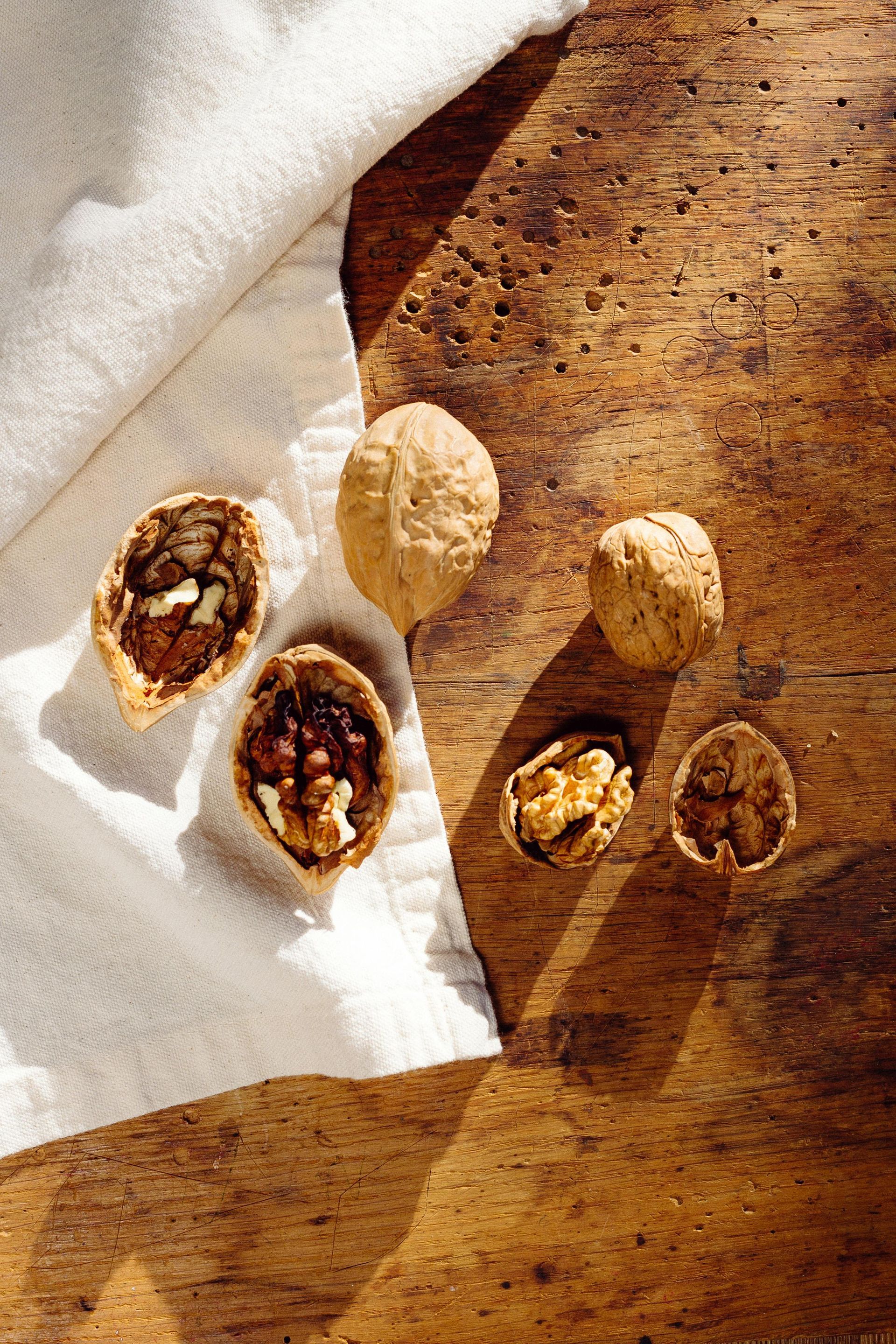 Walnuts on a wooden surface, some cracked open, with a white cloth.