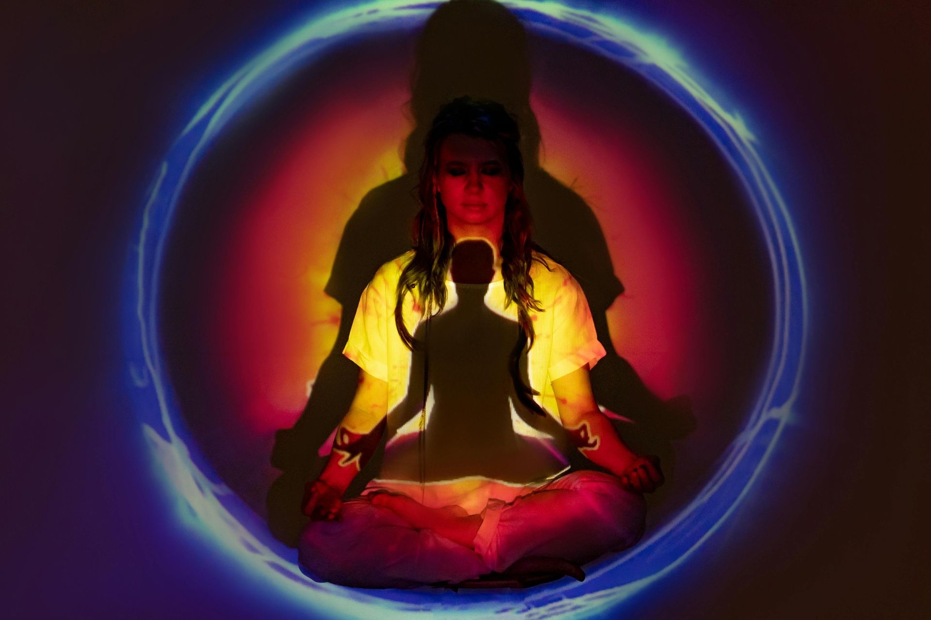 Woman meditating in lotus pose, glowing aura of yellow and blue light.
