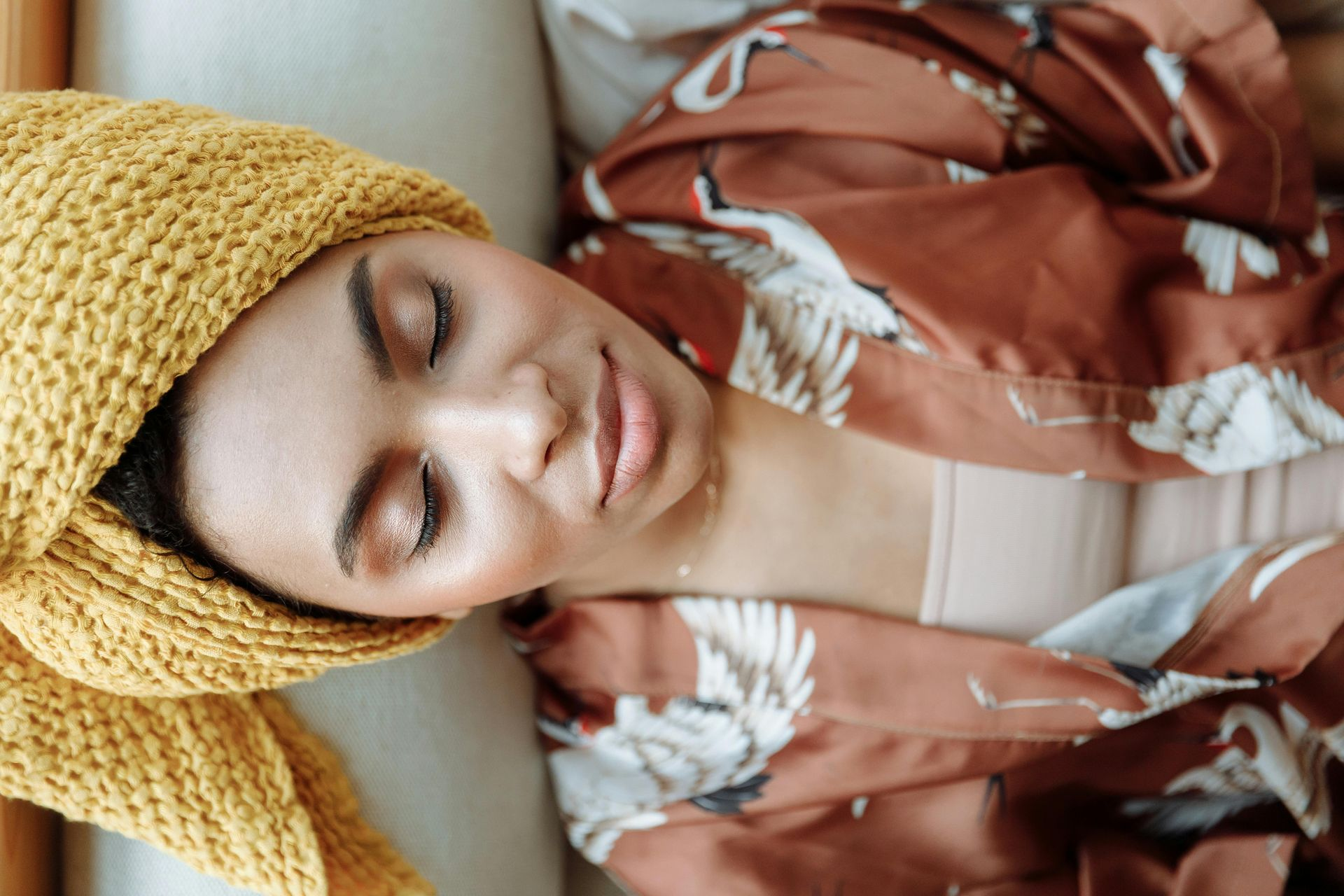 Woman with a towel on her head, wearing a robe, resting indoors.