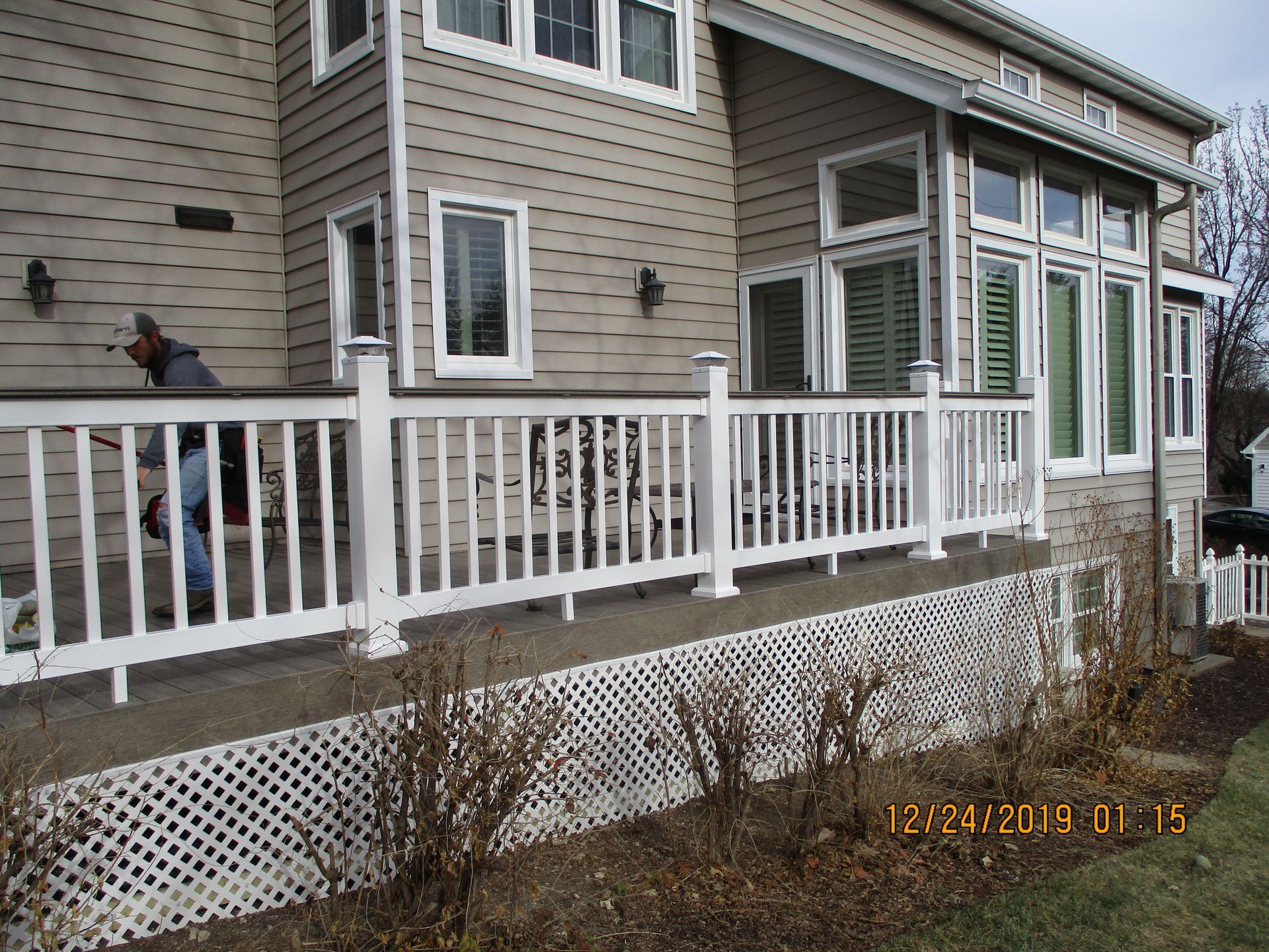 White porch railing on a gray house with a person standing on the left side of the deck.