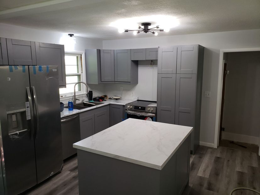 Modern kitchen with stainless steel fridge, gray cabinets, white island, and ceiling fan