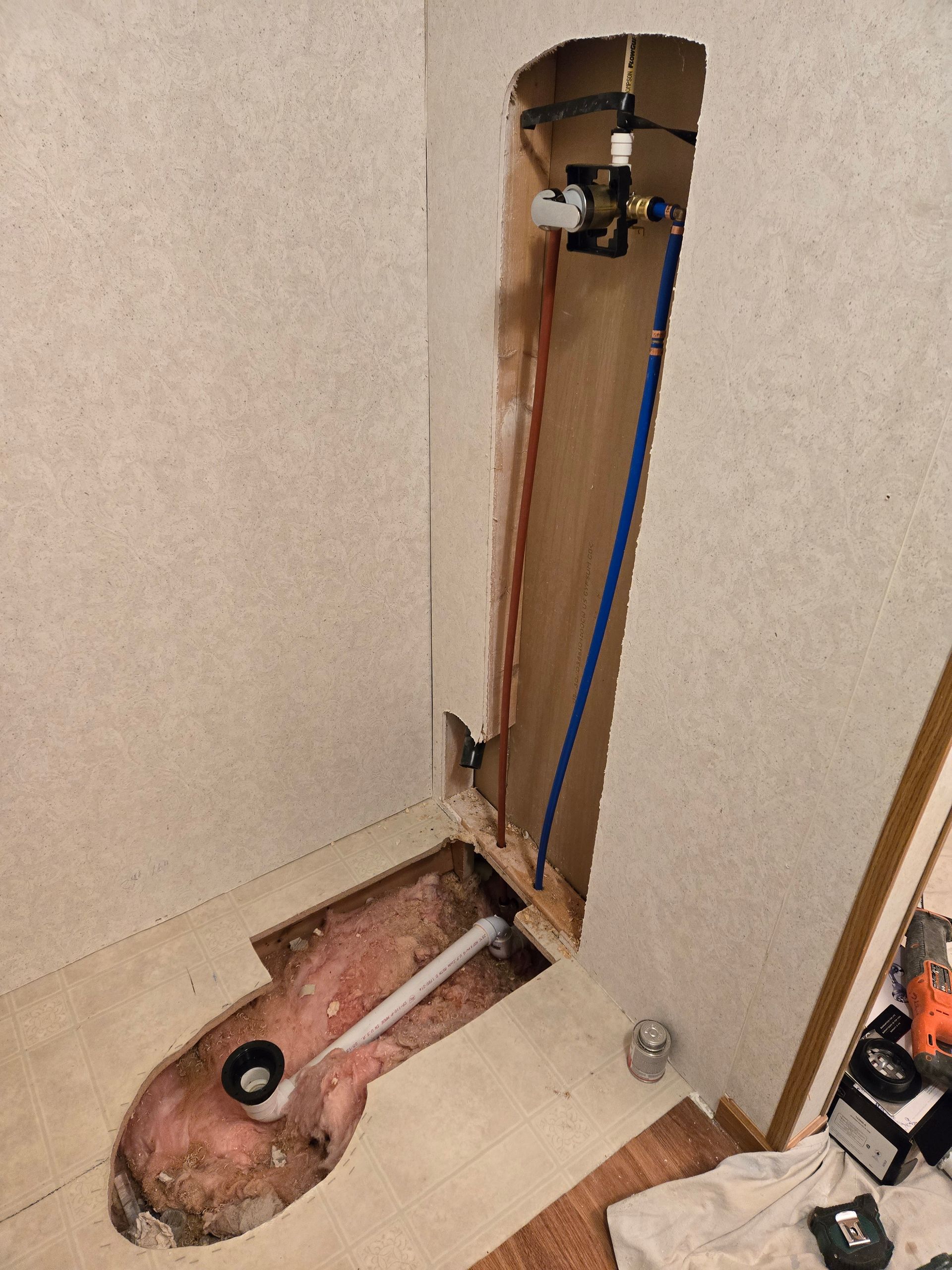 Open wall with exposed plumbing and a vertical copper pipe beside a floor cutout.