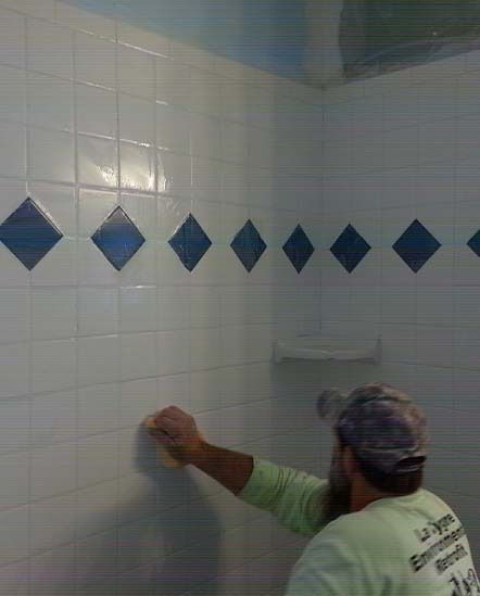 Worker scrubbing white tiled shower wall with blue diamond border tiles