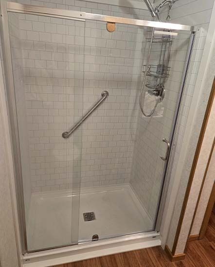 Glass walk-in shower with tiled walls, grab bar, handheld showerhead, and white shower base
