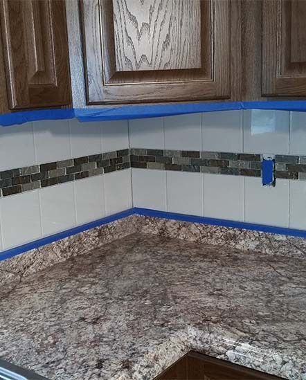 Kitchen countertop and backsplash masked with blue painter’s tape under wooden cabinets during painting prep
