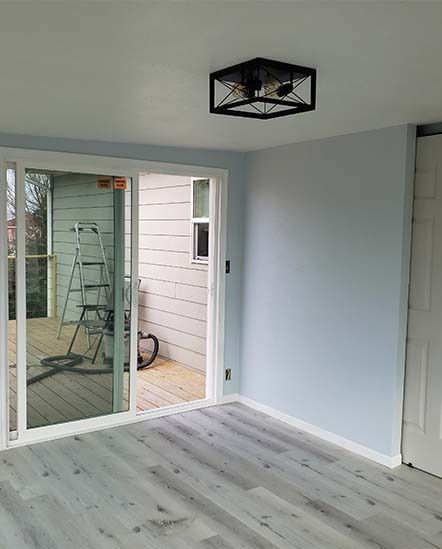 Empty light-gray room with sliding glass door, black ceiling light, and pale wood floor