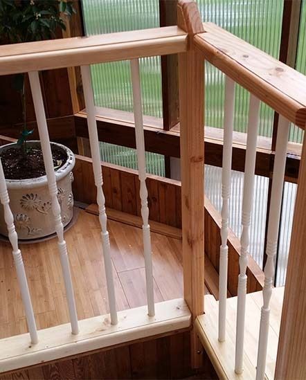 Wooden stair railing with white balusters beside a potted plant in a bright indoor landing
