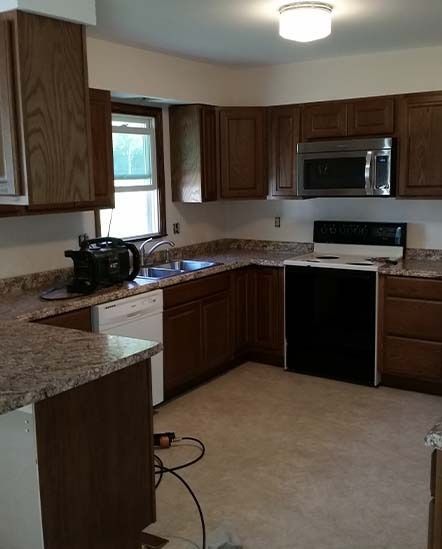 Kitchen with dark wood cabinets, granite counters, stainless microwave, and a black stove on beige tile floor.