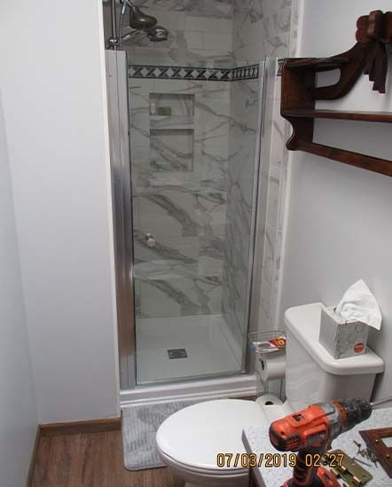 Small bathroom with glass shower stall, toilet, sink, and towel rack on the wall.