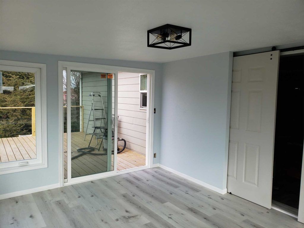 Empty room with light gray walls, white floor, sliding glass doors, and a black ceiling light fixture