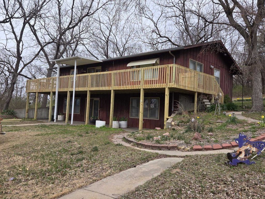 Two-story house with a yellow wooden deck, bare trees, and a leaf-covered yard