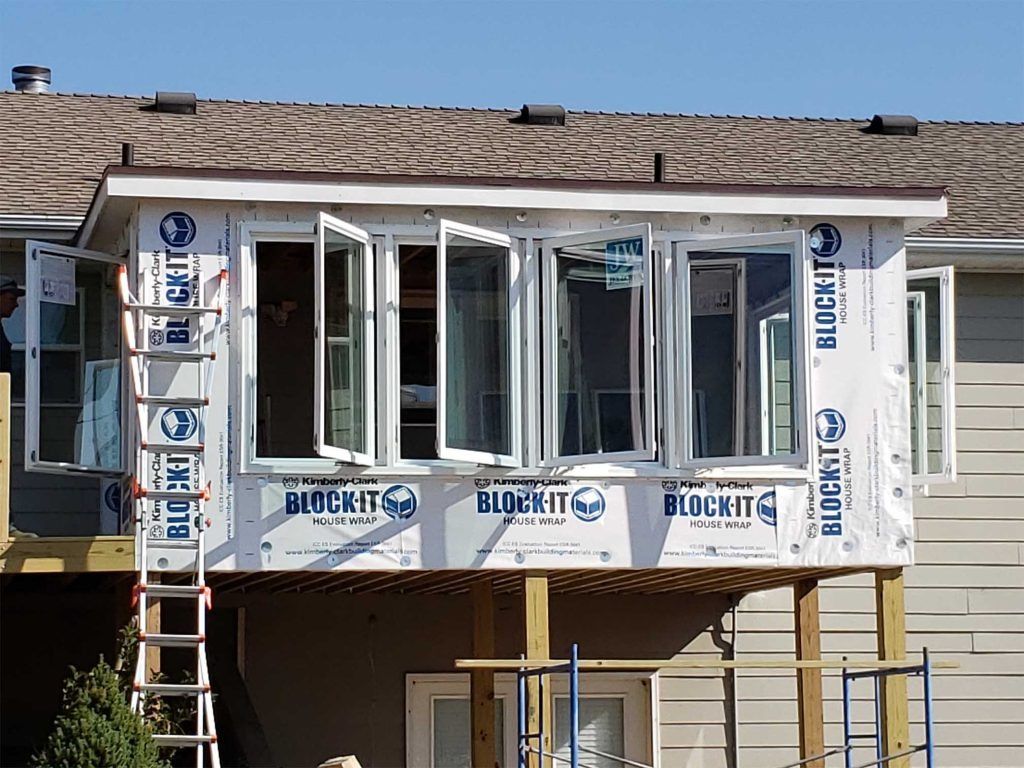 Partially built house with white-framed windows and insulation wrap on an exterior wall